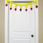 Nestaariya Basanti Toran with yellow gajra, pink roses, green foliage & pearl drops – festive door bandanwar for home entrance
